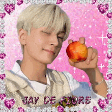 a young man is holding an apple in his hand in front of a pink background with the name jay de fiore written on it .