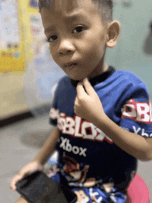 a young boy wearing a blue roblox xbox shirt looks at the camera