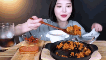 a woman is eating food with a wooden spoon from a pan