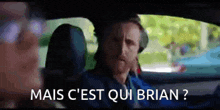 a man is sitting in the driver 's seat of a car with the words mais c'est qui brian written on the screen .