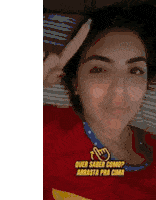 a woman in a red shirt is laying on a bed and giving a peace sign .