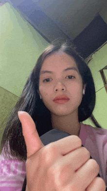 a woman giving a thumbs up sign with a pink shirt on