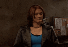 a woman wearing a leather jacket and a blue shirt is standing in front of a bulletin board
