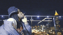 a person is smoking a cigarette in front of a city at night .