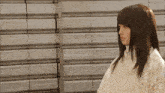 a woman in a white sweater stands in front of a wall of bricks