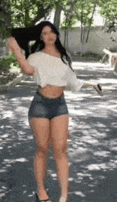 a woman in a white crop top and denim shorts is standing on a sidewalk .