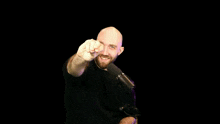a bald man with a beard is standing in front of a microphone and waving at the camera .
