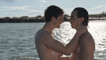 two shirtless men are hugging in the water and looking at each other