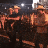a group of men in cowboy hats are dancing in front of a crowd at a concert .