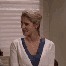 a woman in a white cardigan and blue top smiles