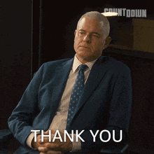 a man in a suit and tie is sitting in front of a sign that says " thank you "