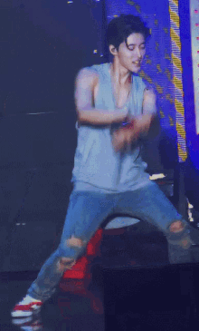 a man in a blue tank top and ripped jeans is dancing on stage