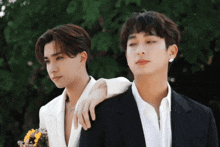a couple of men standing next to each other with one holding a bouquet of flowers