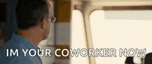 a man wearing glasses is standing in front of a window and says `` i 'm your coworker now ''