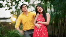 a man in a yellow shirt and a woman in a red dress are standing next to each other and laughing .