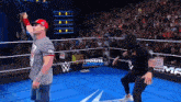 a man in a hoodie stands in a wrestling ring next to a man in a gray shirt