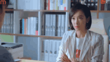 a woman in a striped jacket is sitting at a desk in front of a bookshelf .