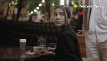 a woman sits at a table with a tencent video logo in the corner