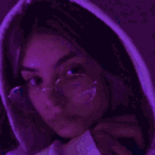a close up of a girl wearing glasses and a hoodie in a purple room .