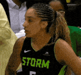 a female basketball player wearing a black and green storm jersey is sitting in the stands .