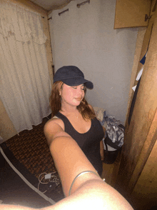 a woman wearing a black tank top and a blue hat takes a picture of herself