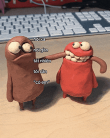 two clay figures are standing next to each other on a table with a keyboard in the background and one of them says " có em "