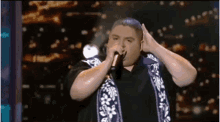 a man is singing into a microphone with his hands on his head