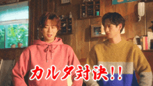 a man in a pink hoodie stands next to another man in a yellow sweater with chinese writing on it