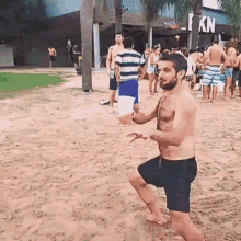 a man without a shirt is standing on a sandy beach in front of a crowd .