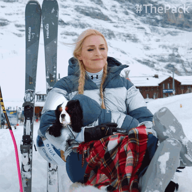 a woman sits in the snow holding a dog and a pair of skis that say head
