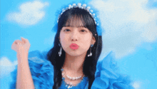 a girl wearing a blue dress and pearls is blowing a kiss at the camera