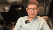 a man wearing glasses is sitting in a car with a microphone attached to his neck