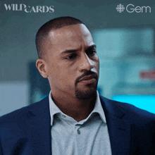 a man in a suit and a gray shirt is standing in front of a gem logo