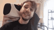 a man with a beard is sitting on a bed with a pillow on his head .