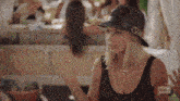 a woman wearing a hat and a black tank top is talking to someone .