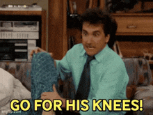 a man in a green shirt and tie is sitting on a couch and saying go for his knees
