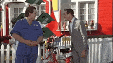 a man in a suit and tie is standing next to a man in a blue jumpsuit .