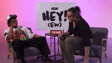 two men sit in front of a sign that says hey ew