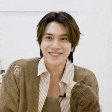 a man wearing a brown sweater and striped shirt smiles for the camera