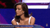 a woman in a white tank top is sitting in front of a screen that says " entrevias "