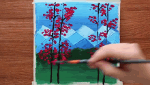 a person is painting a landscape with trees and mountains in the background .