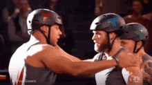 three men wearing helmets are hugging each other and nbc is behind them