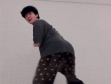 a man wearing a gray t-shirt and black pants is dancing in a room .
