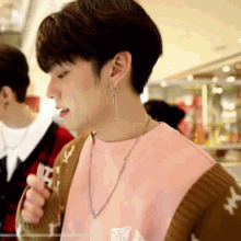 a young man wearing a pink shirt and a brown cardigan is holding something in his hand