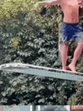 a shirtless man is standing on a trampoline in front of trees .