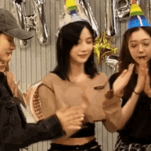 a woman wearing a birthday hat is clapping her hands with two other women