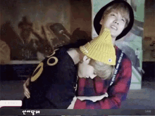 a man wearing a yellow hat is hugging another man wearing a black shirt that says j hope