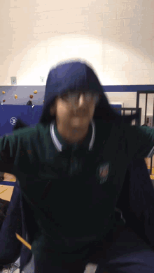a person wearing a green shirt and a blue hoodie with the number 1 on the wall behind them