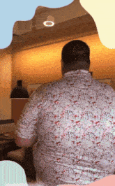 a man wearing a floral shirt sits in a room