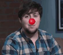 a man with a red clown nose is wearing a plaid shirt